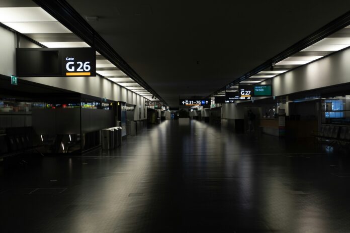 An empty, dimly lit airport terminal at night, with lit gate signs and a polished floor, for an essay on overcoming fear of flying.