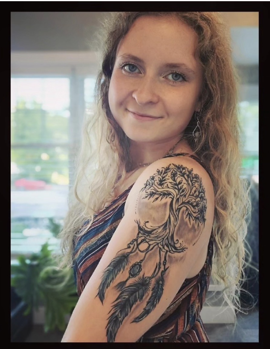 Abigail Ouellette smiling, showing the healed Tree of Life dreamcatcher tattoo covering her upper arm.